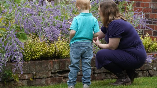 A woman and child look at the border in the garden of Mompesson House. She is wearing a dark blue dress and he has light hair and is wearing a light blue top. He is around five.